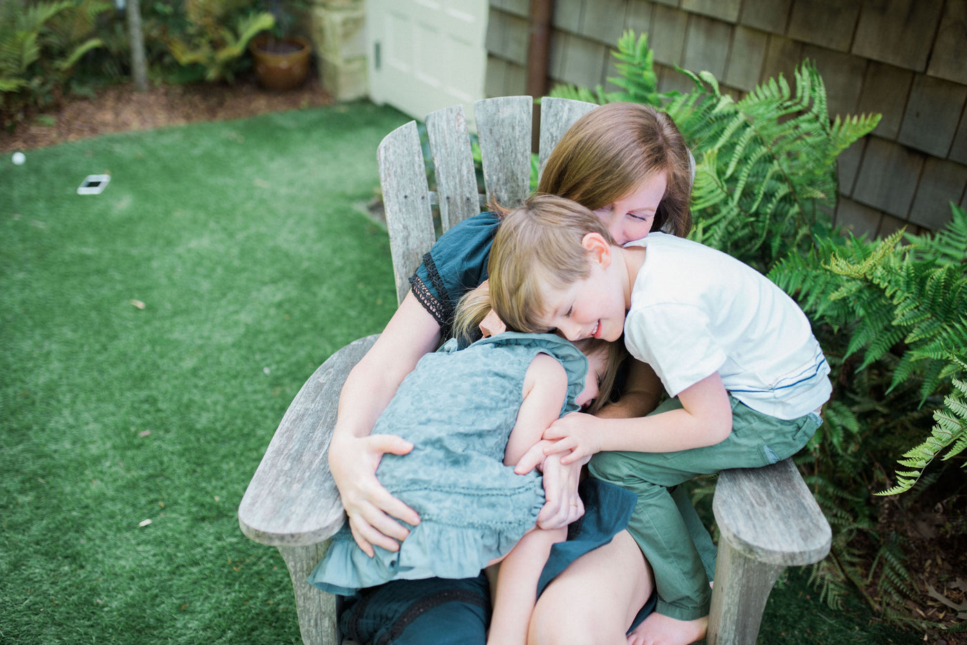 Woman in a navy dress with black lace inserts with two kids in her lap. The girl is wearing a blue embroidered dress. The boy is in a white embroidered t-shirt and green pants.