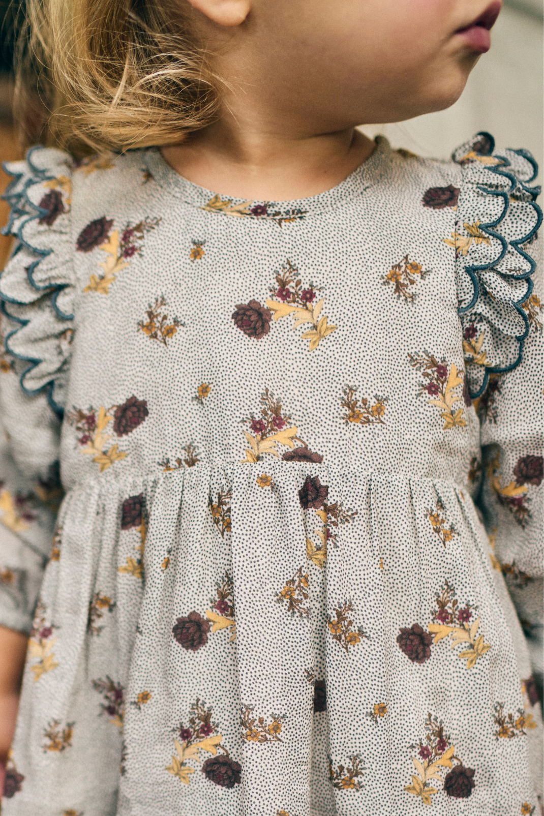 Close-up of a child wearing a floral dress with ruffled sleeves.