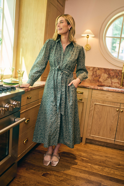 Woman in a green patterned dress standing in a kitchen.