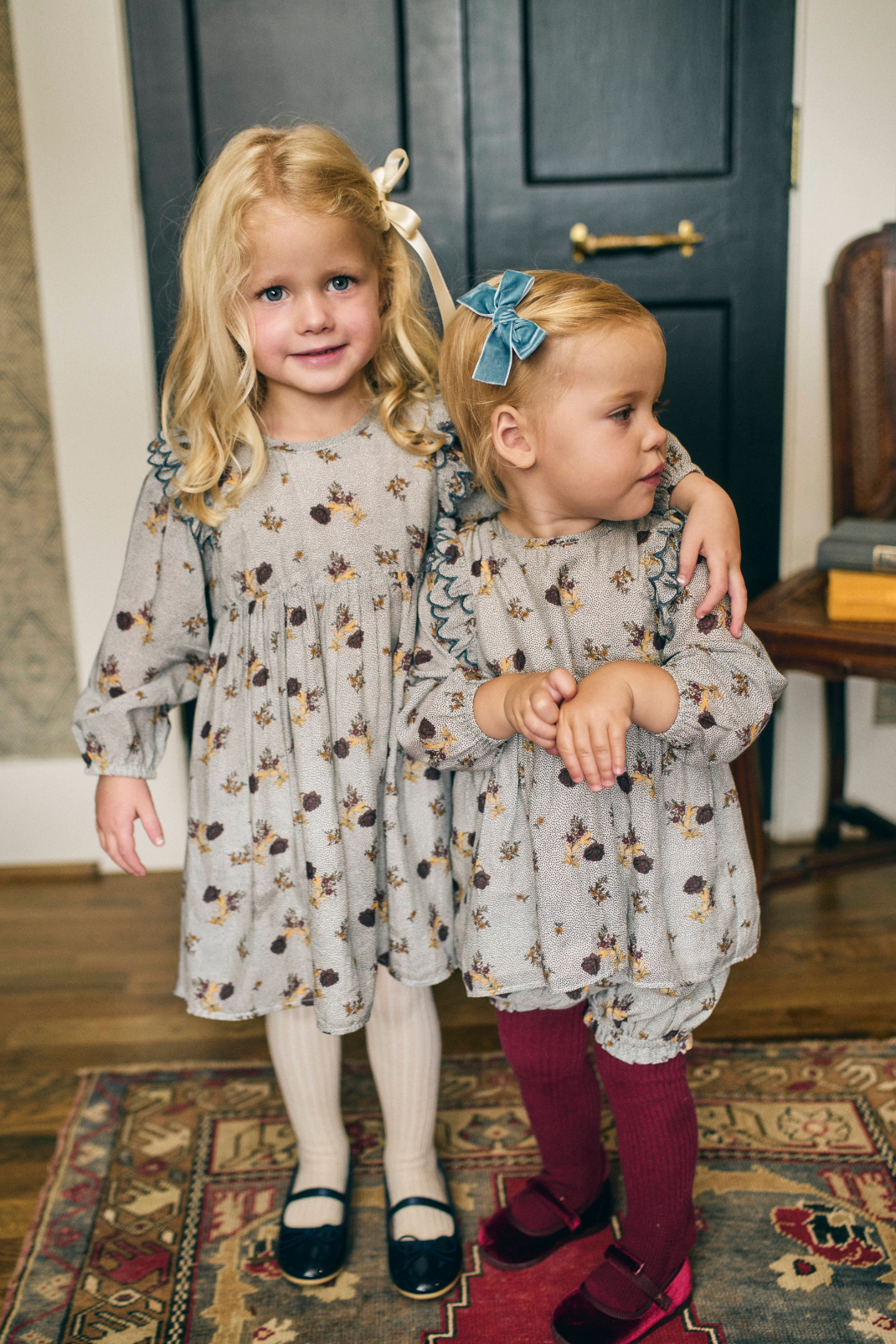 Two young girls in matching dresses standing in a room with a dark blue door.