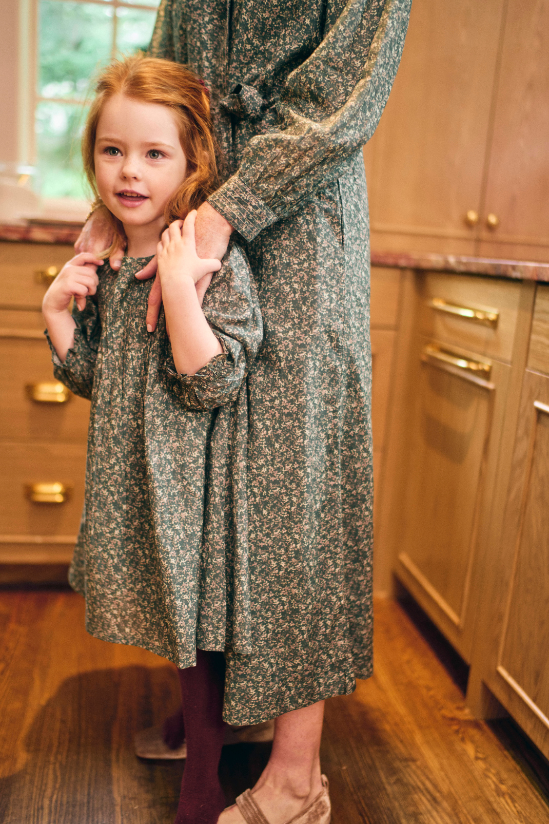 Woman and child in matching floral dresses standing in a kitchen.