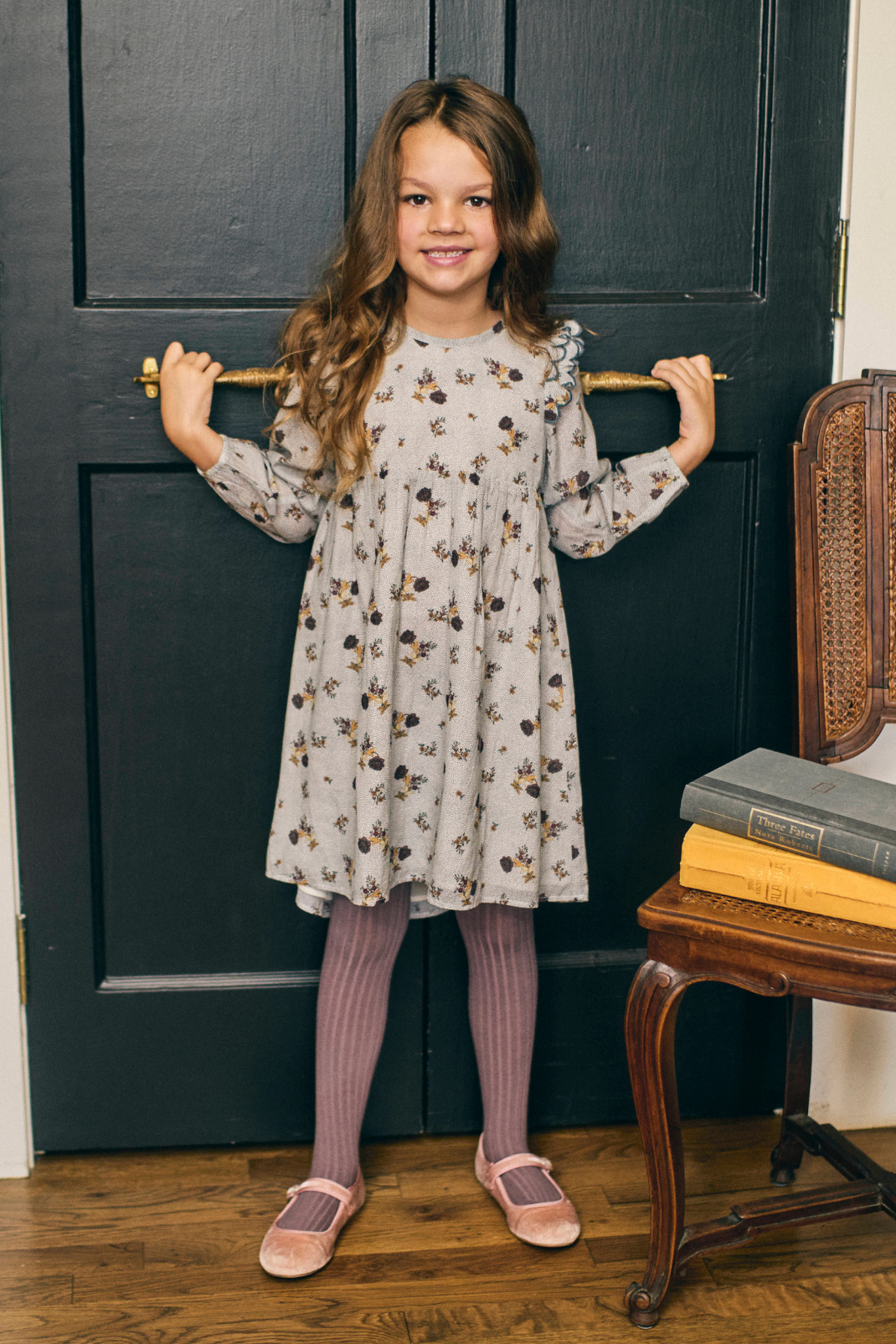 Young girl in a floral dress standing in front of a dark door.