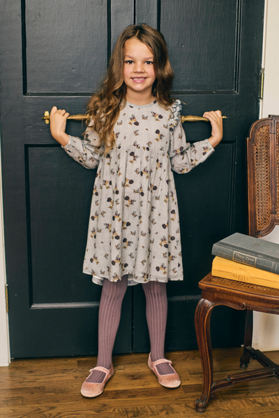 Young girl in a floral dress standing in front of a dark door.