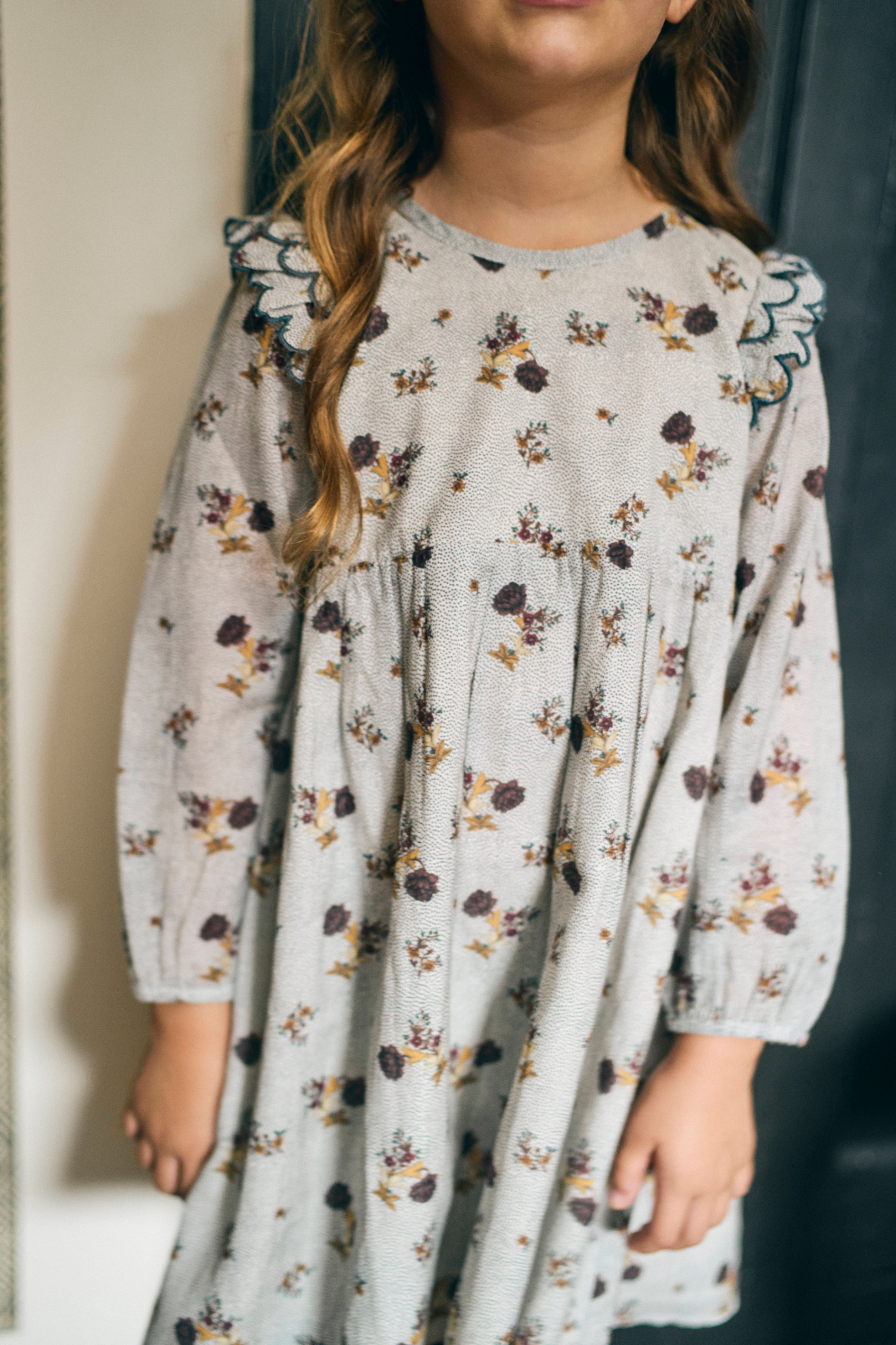 Child wearing a floral dress with long sleeves against a neutral background