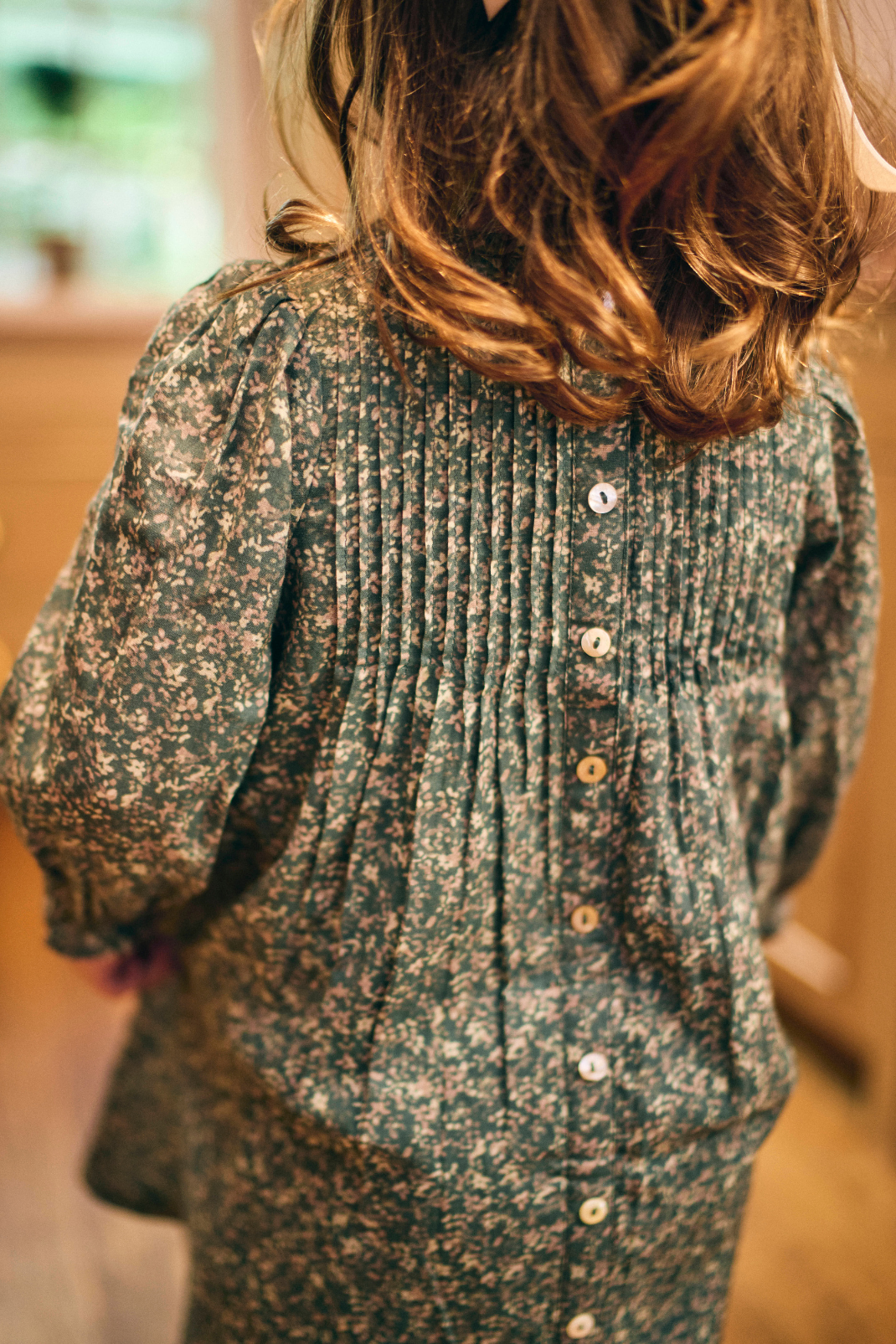 Little girl wearing a patterned green dress with buttons down the back