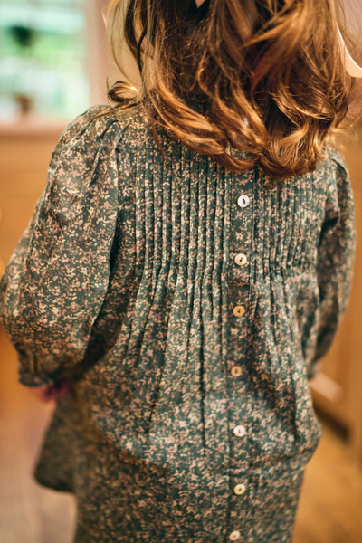Little girl wearing a patterned green dress with buttons down the back