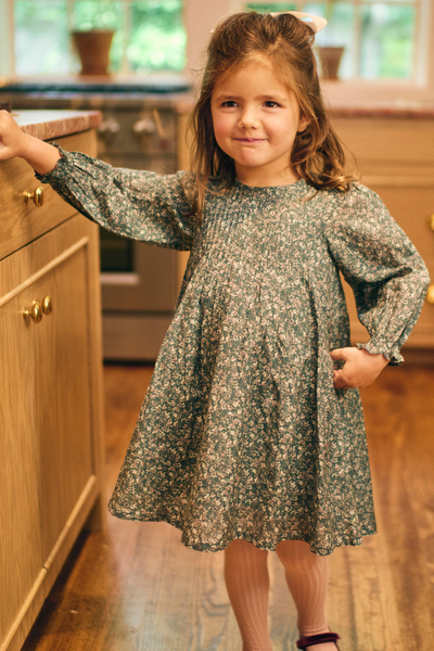 Young girl in a floral dress standing in a kitchen.