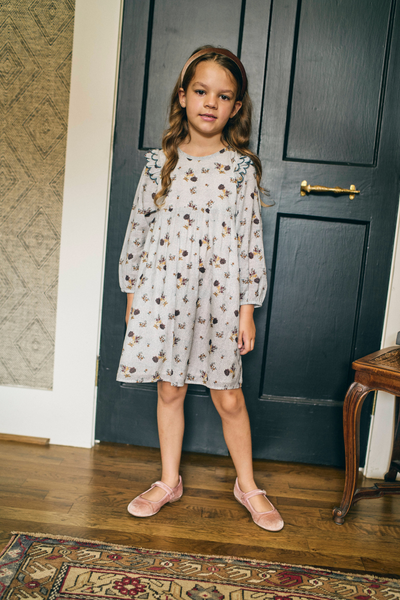 Young girl in a floral dress standing in front of a dark blue door.