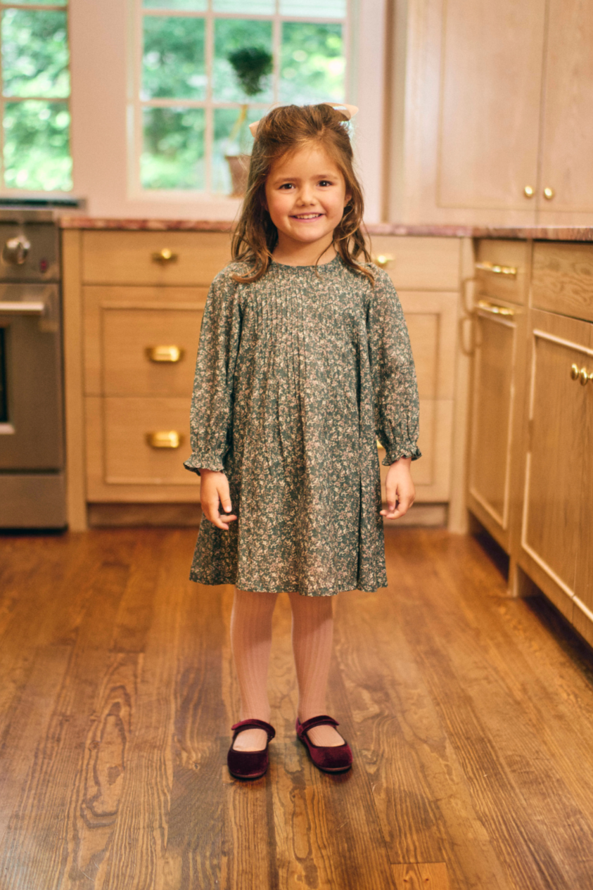Young girl standing in a kitchen with wooden floors and cabinets