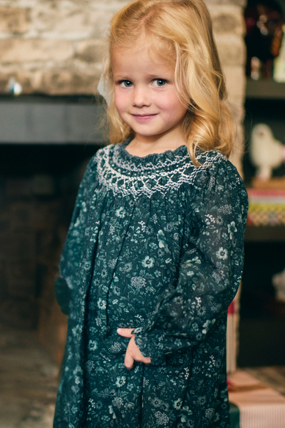 Young girl wearing a dark green dress with lace details in a cozy indoor setting.