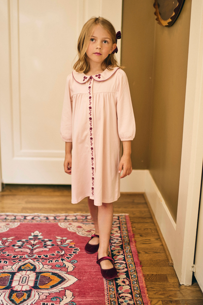 Young girl in a pink dress standing in a room with a patterned rug.