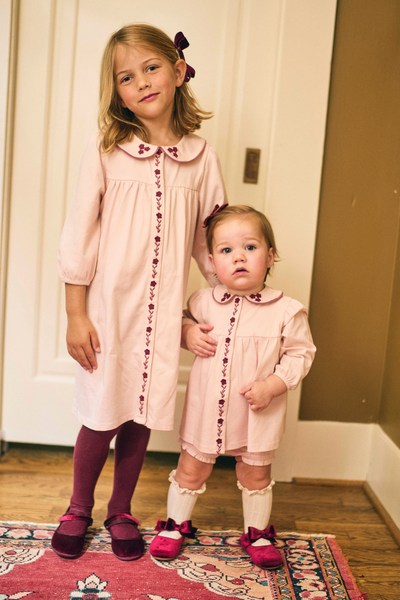 Two young girls in matching pink dresses standing on a patterned rug.
