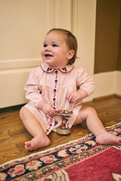 Child in a pink dress sitting on a wooden floor with a colorful rug.