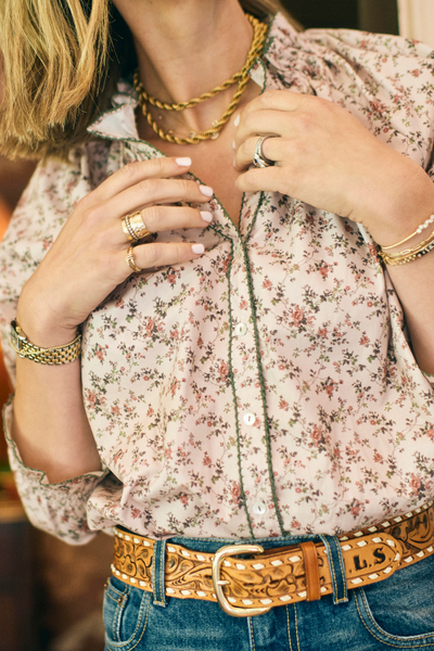 Person wearing a floral blouse, gold jewelry, and a belt with a large buckle.