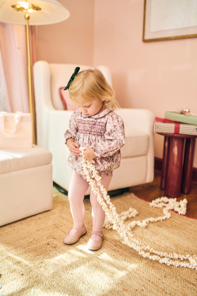 Young girl playing with a long string of pearls in a decorated room.