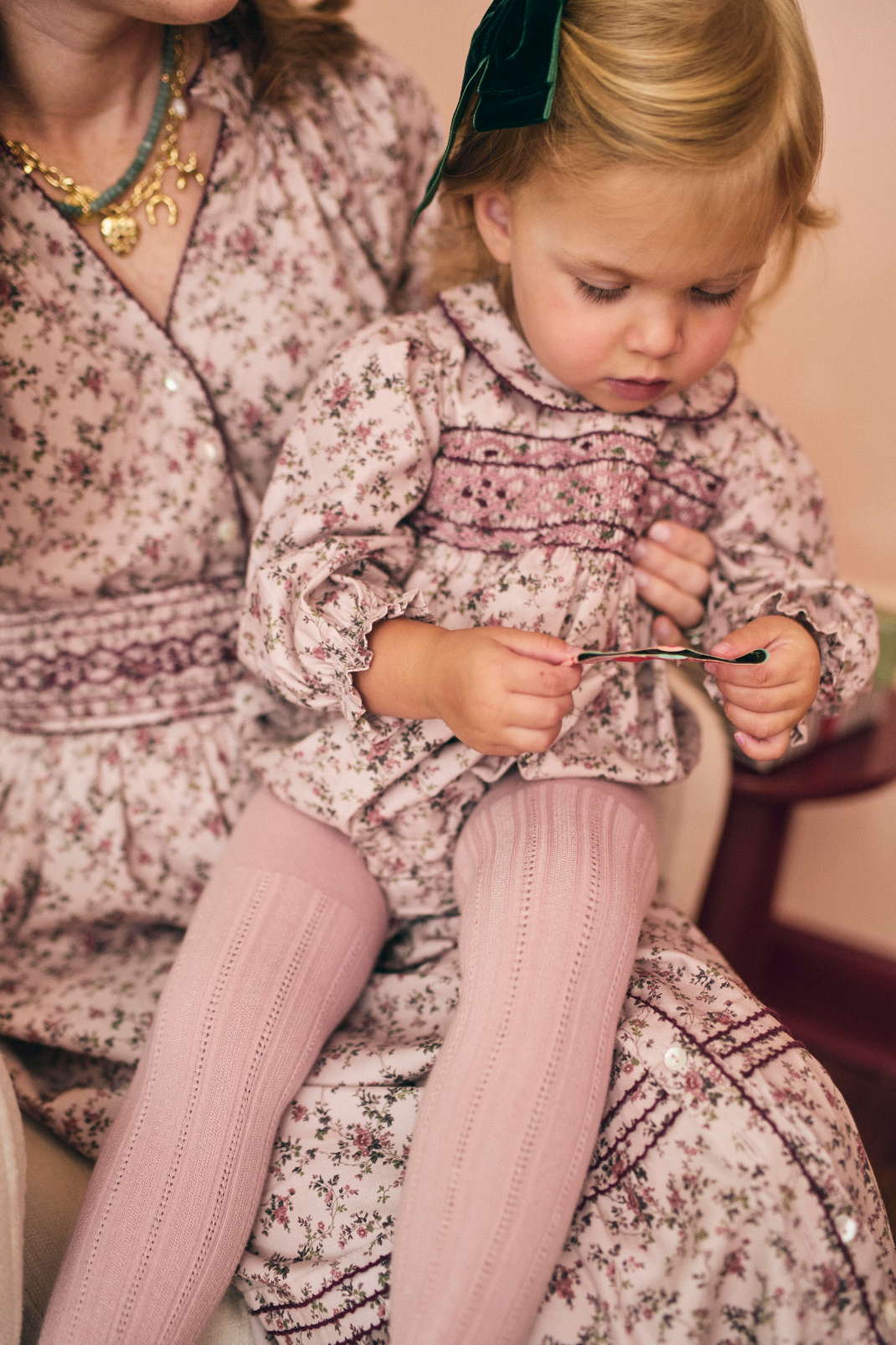 Young child in a floral dress and pink tights sitting on a woman's lap.