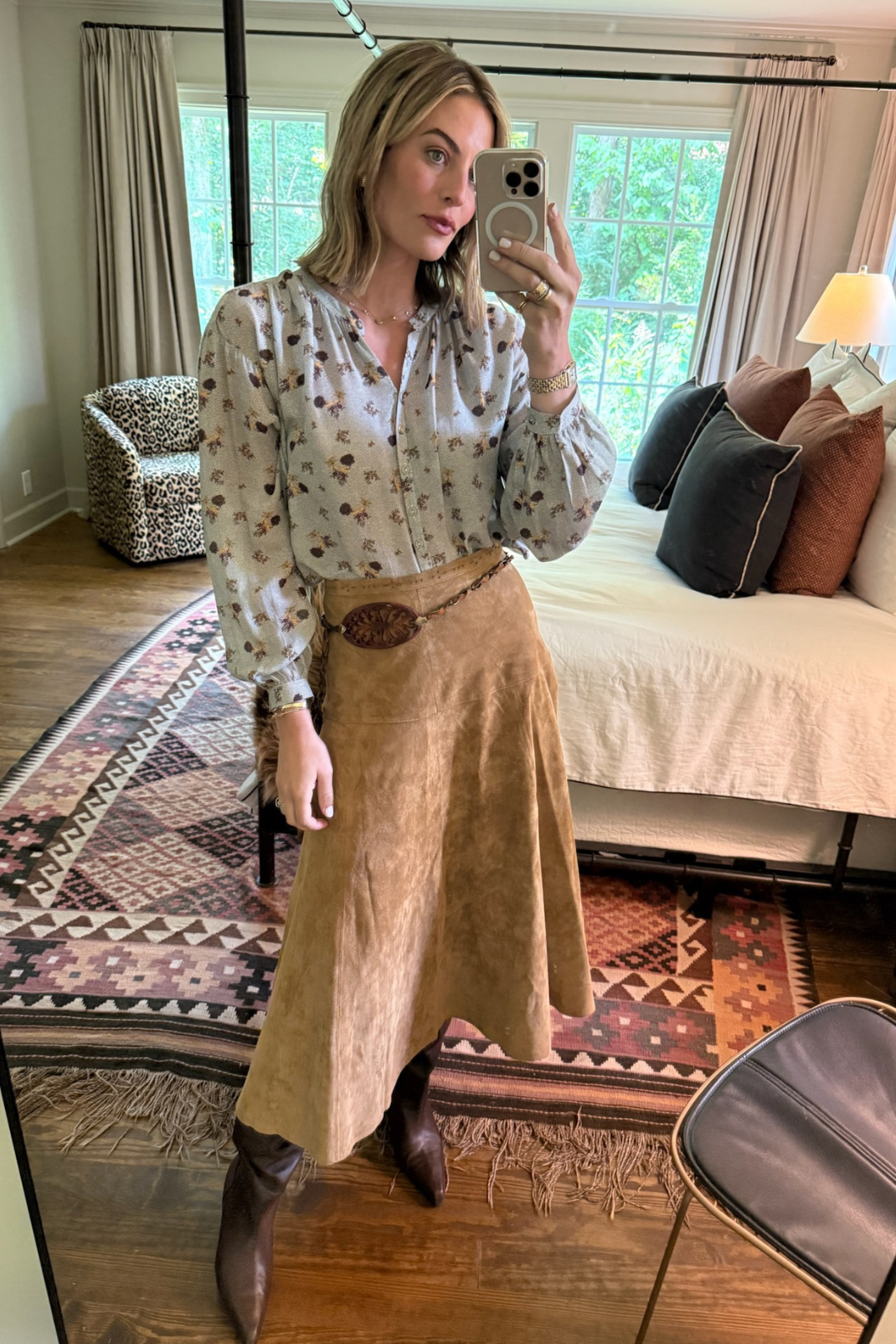 Woman taking a mirror selfie in a room with a bed and window in the background