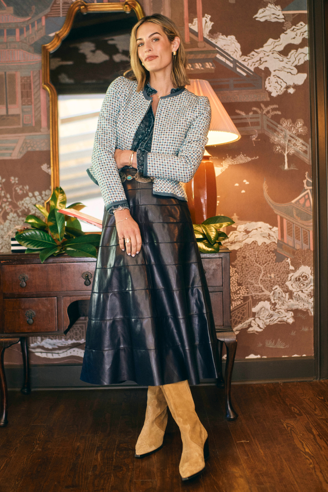 Woman in a stylish outfit with a leather skirt and tweed jacket in an elegant room.