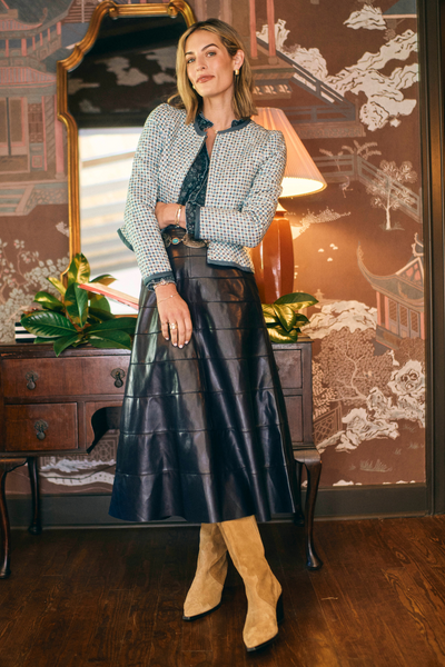 Woman in a stylish outfit with a leather skirt and tweed jacket in an elegant room.