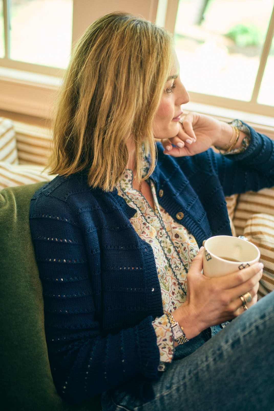 Woman sitting on a couch holding a mug, wearing a blue cardigan.