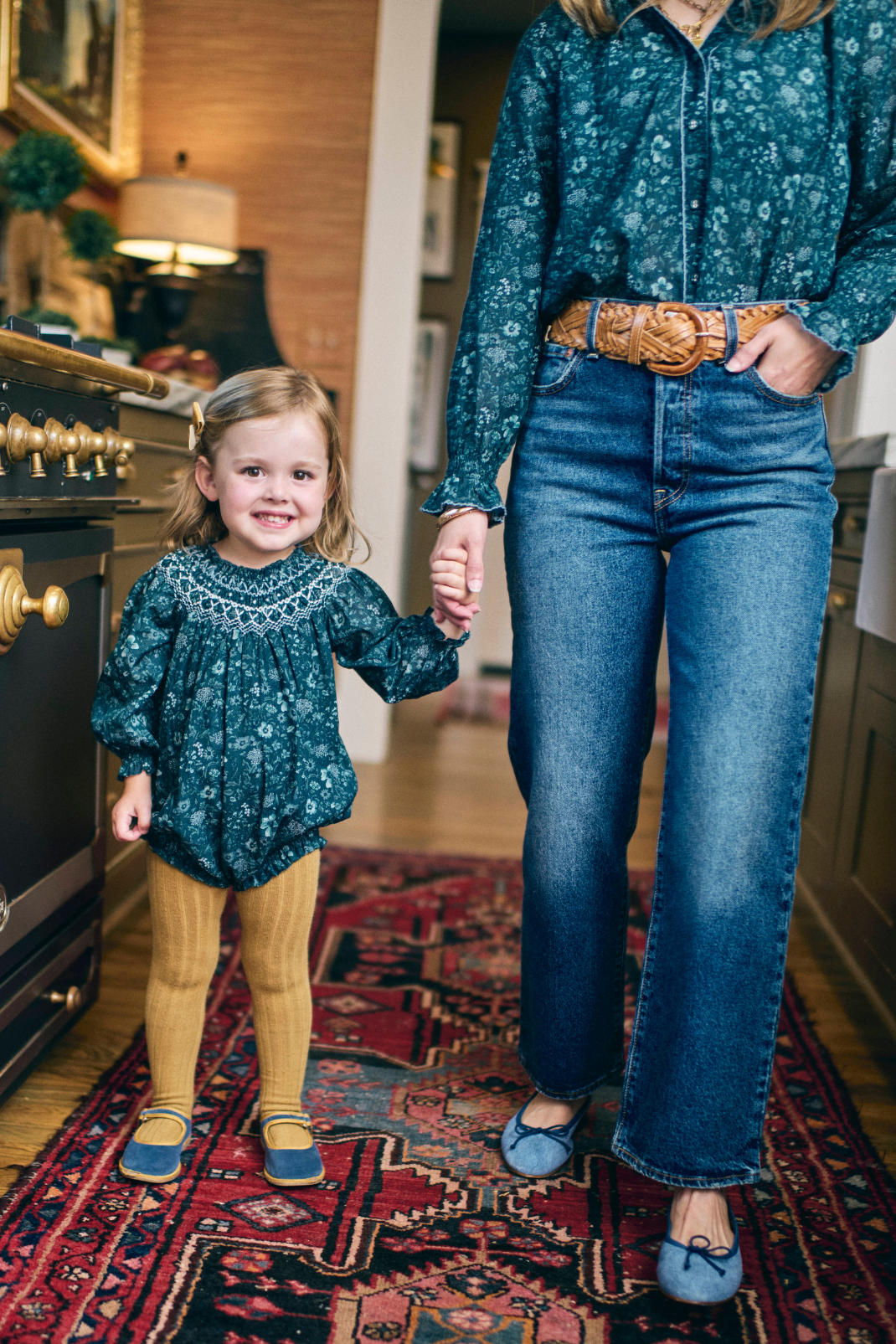 Woman and child holding hands in a room with a patterned rug.