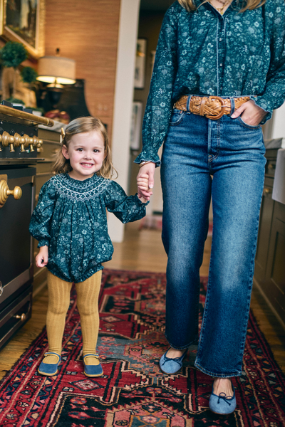 Woman and child holding hands in a room with a patterned rug.