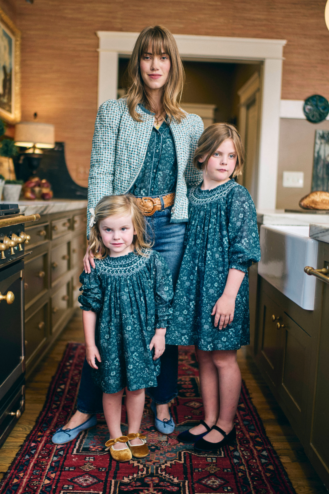 Woman and two young girls in matching teal outfits standing in a kitchen.