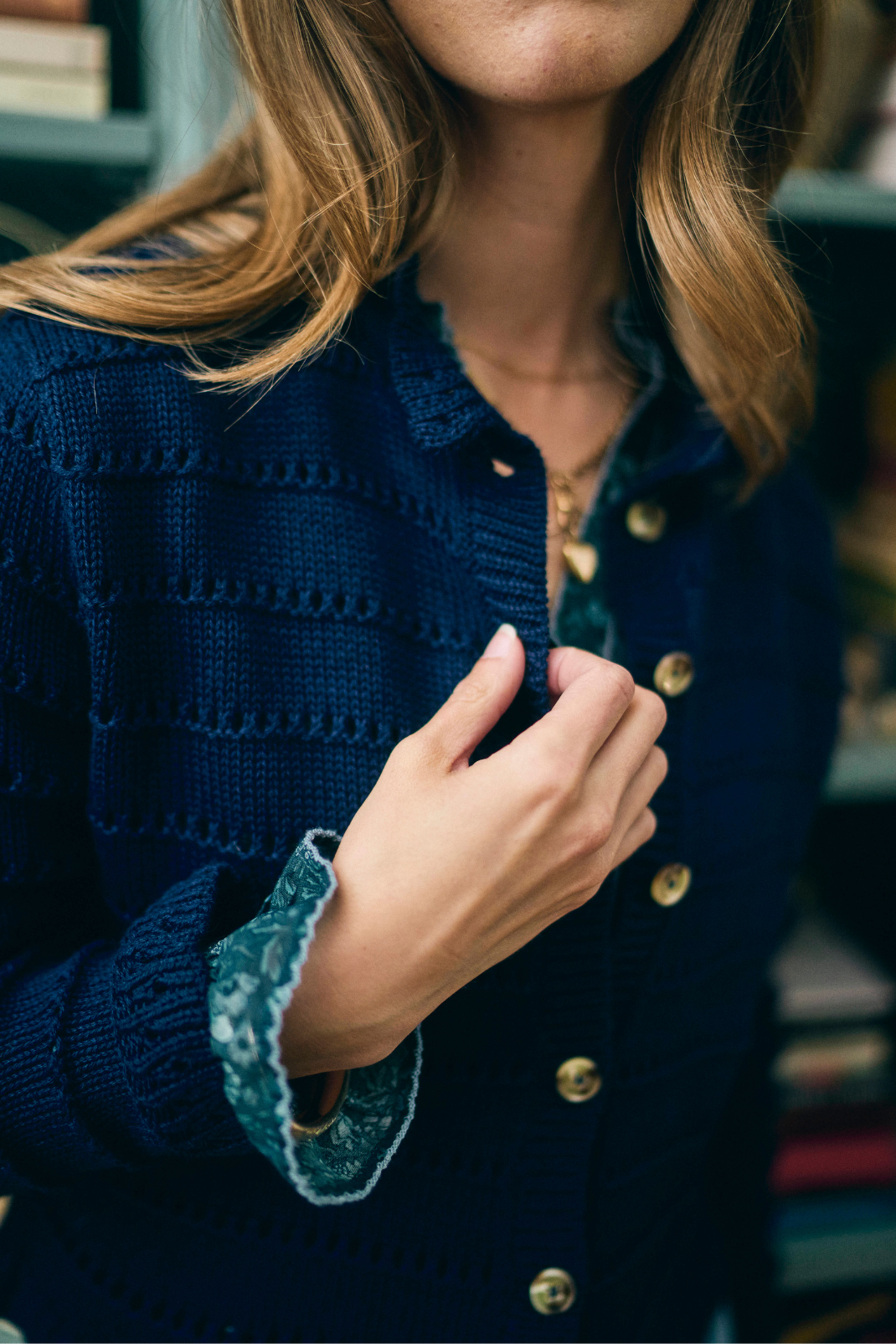 Person wearing a blue textured cardigan with wood buttons, indoors.