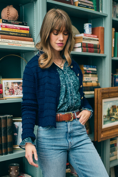 Woman standing in a blue cardigan and blue floral top next to bookshelves and books in the background