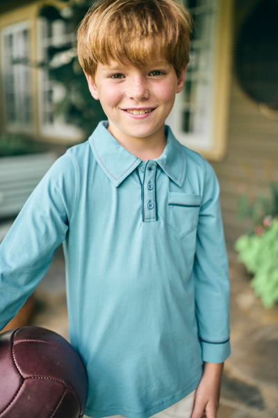 Young boy in a blue long sleeve polo shirt holding a soccer ball outdoors.