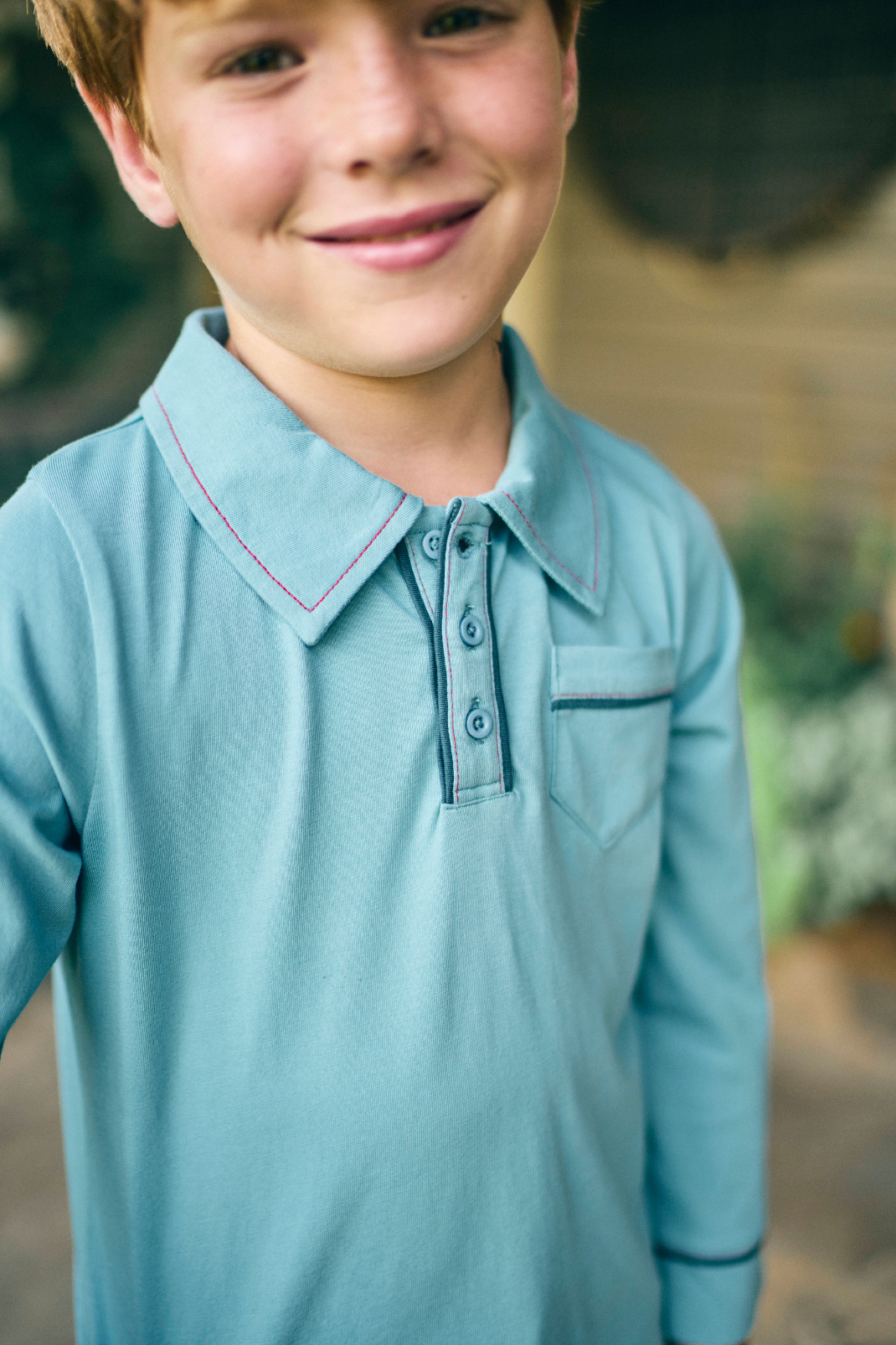 Young boy wearing a light blue polo shirt with a blurred outdoor background