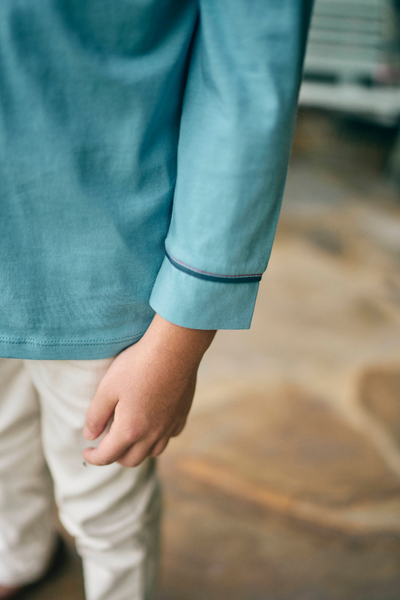 Close-up of a person wearing a light blue shirt with white pants on a blurred background