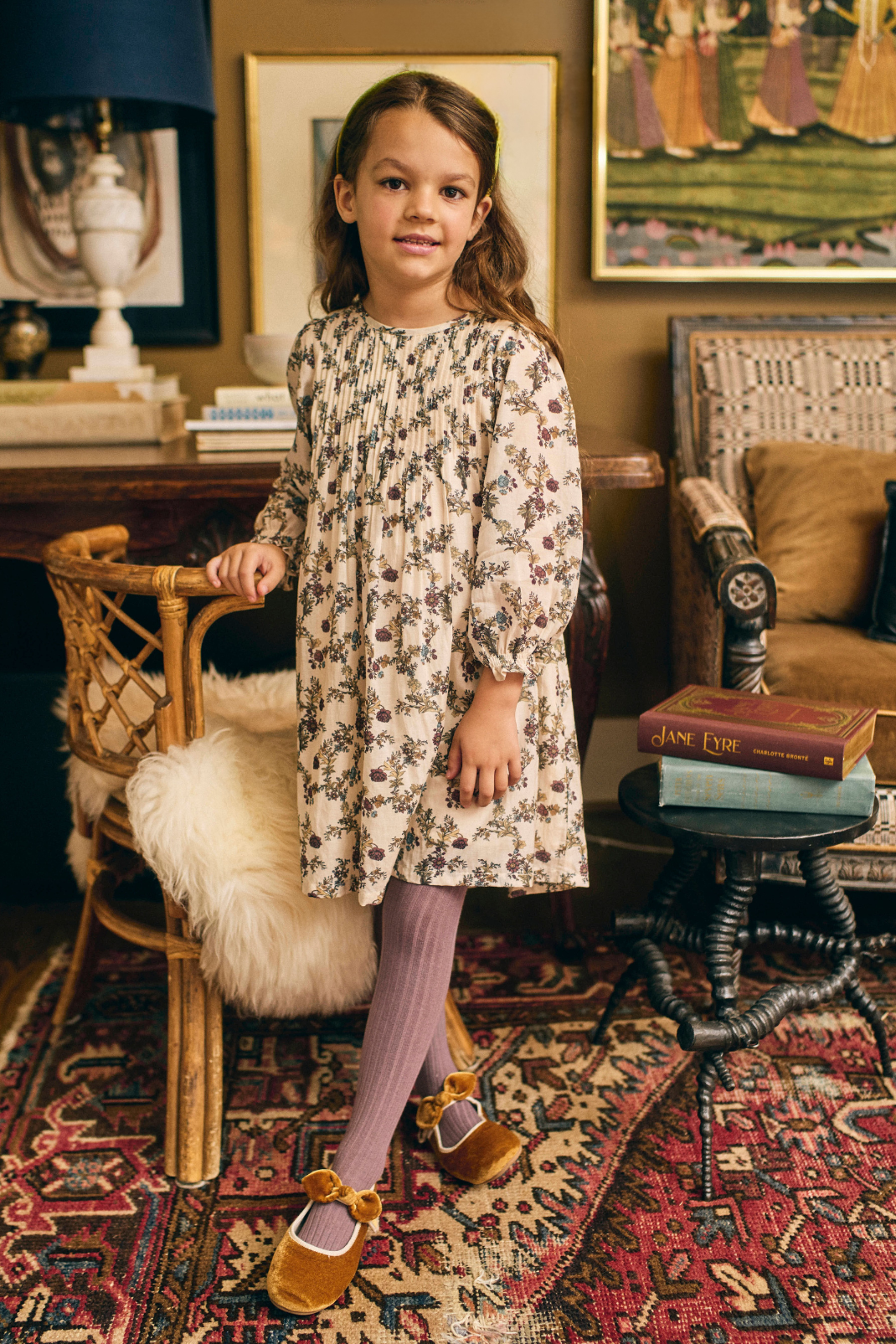 Young girl in a floral dress standing in a room with vintage decor.