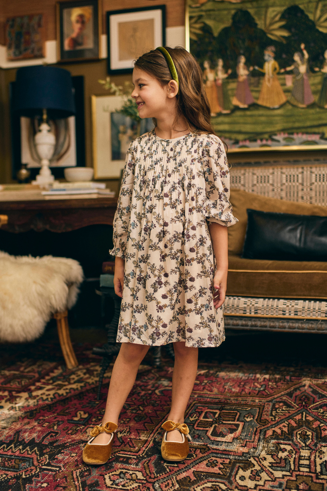 Young girl in a floral dress standing in a room with vintage decor