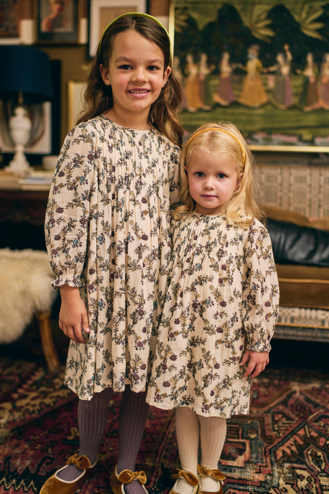 Two young girls in floral dresses standing in a room with decorative elements.