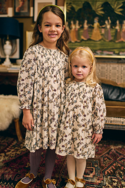 Two young girls in floral dresses standing in a room with decorative elements.