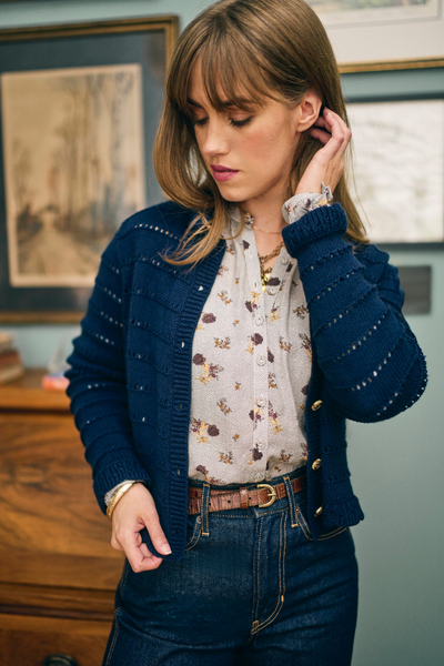 Woman wearing a blue cardigan over a floral blouse in an indoor setting.