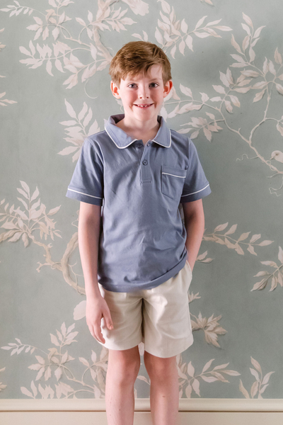Little boy wearing blue polo shirt with white piping and stone colored shorts
