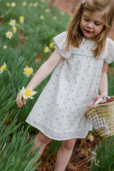 Lifestyle shot of a little girl picking flowers wearing the Dolly Dress