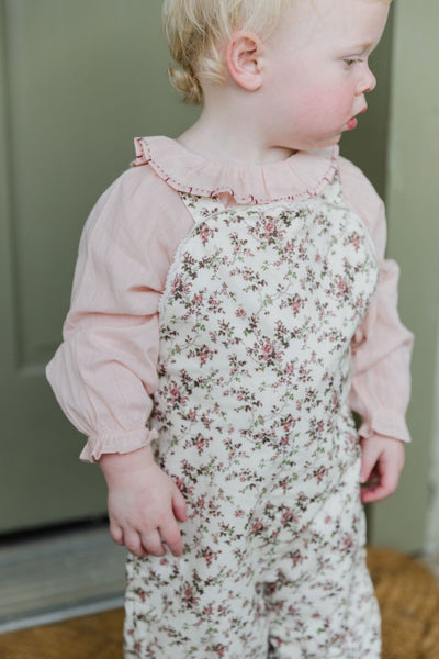 Lifestyle shot of a little girl standing outside wearing the Shaw Playsuit in Overgrown Floral and the Bea Top in Rose Smoke