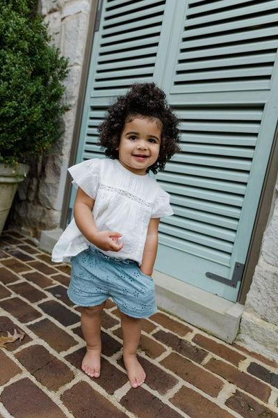 Lifestyle shot of little girl outside wearing a short sleeve white top and blue shorts