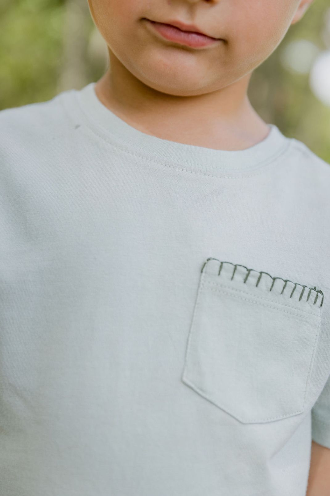 Close up lifestyle shot of a little boy wearing the Henry T-Shirt in Pigeon with Thyme