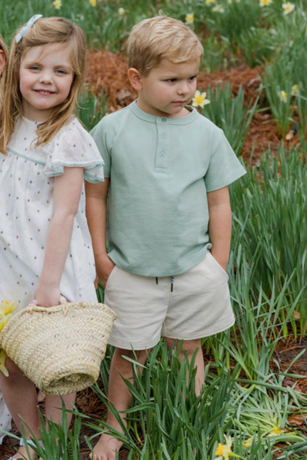 Lifestyle image of a little boy and girl standing outside in a field of flowers