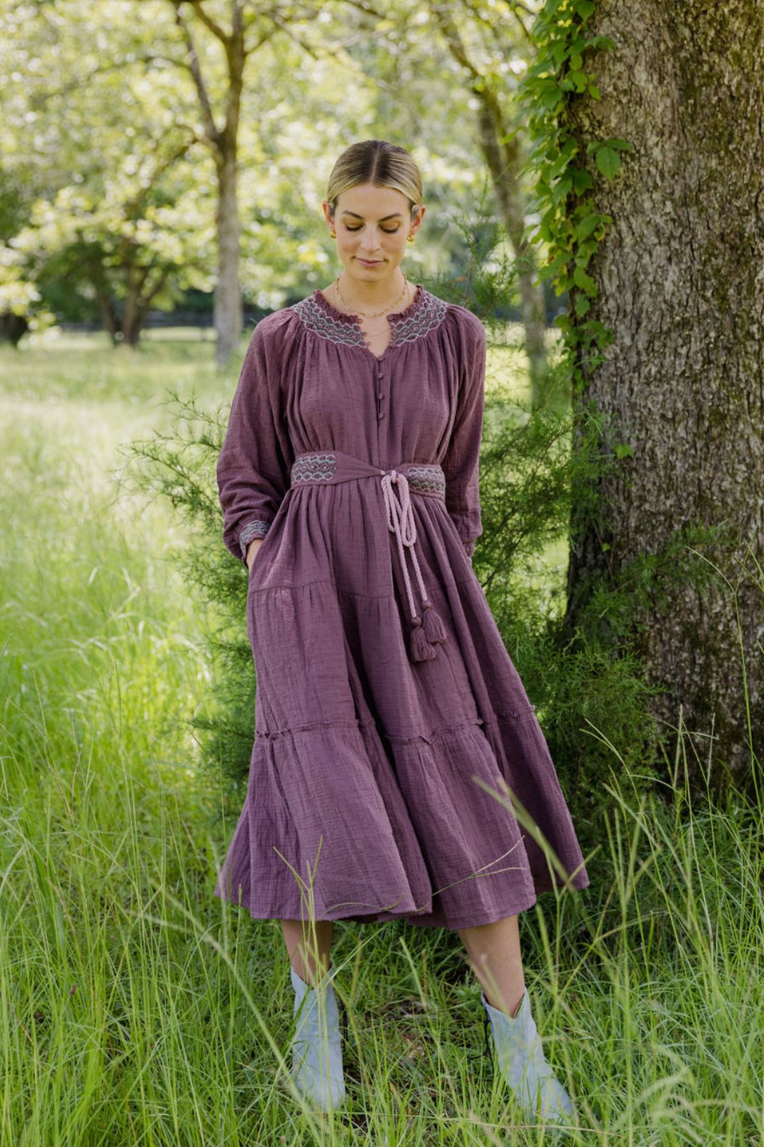 Lifestyle image of a woman standing outside in a field of grass wearing the Lucy Dress in Vintage Wine