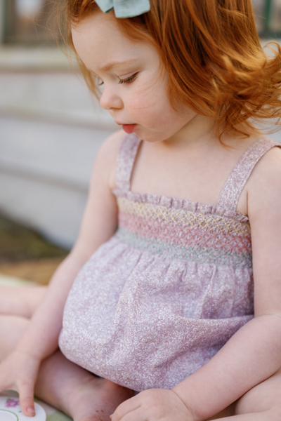 Little girl sitting down outside wearing the Rosie Baby Set in Scattered Blooms
