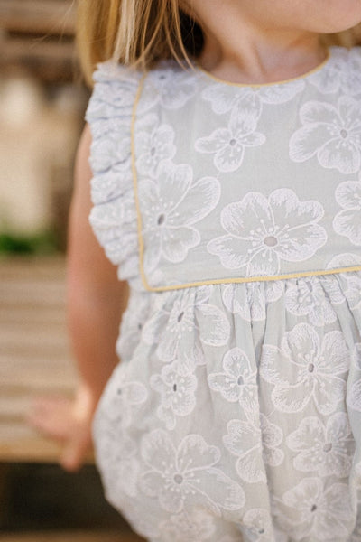 Close up of a little girl wearing the Elizabeth Playsuit in Sky Anemone Embroidery
