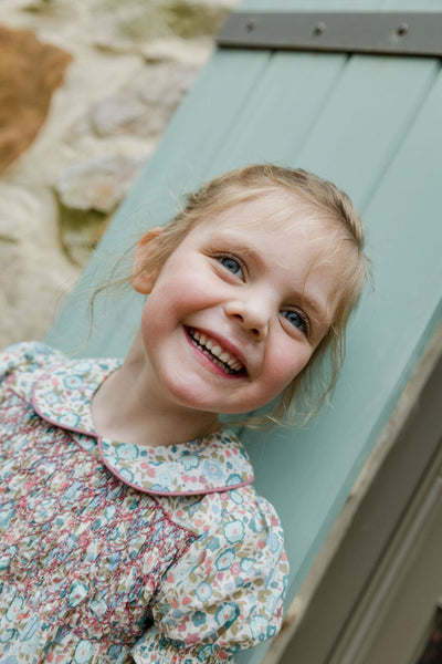 Little girl outside leaning against a door wearing the Emmy Dress in floral breeze