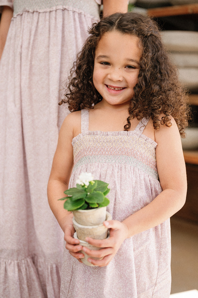 Close up of a little girl holding a plant wearing the Rosie Dress in Scattered Blooms