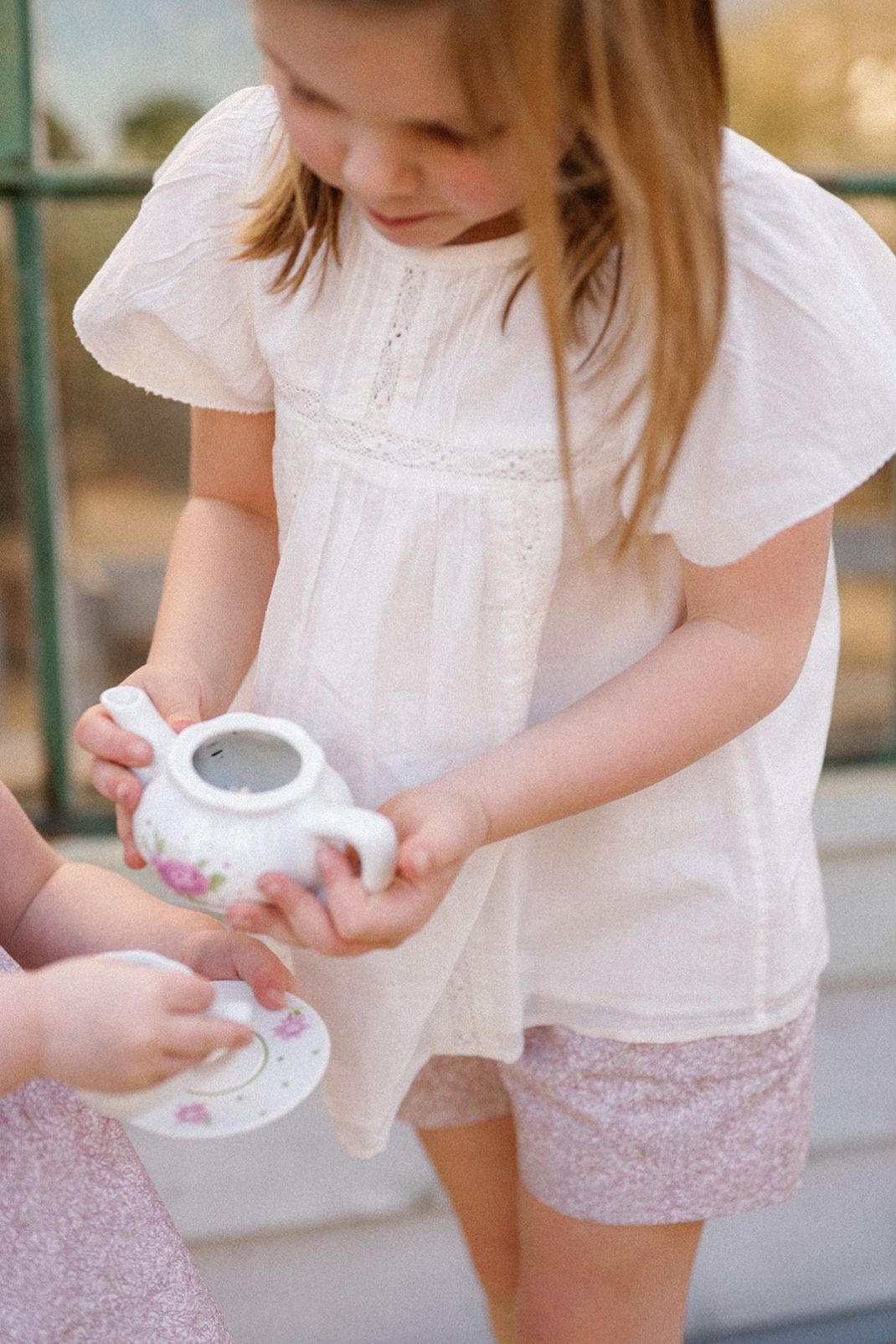 Little girl holding a tea pot wearing our Mae Short in Scattered Blooms