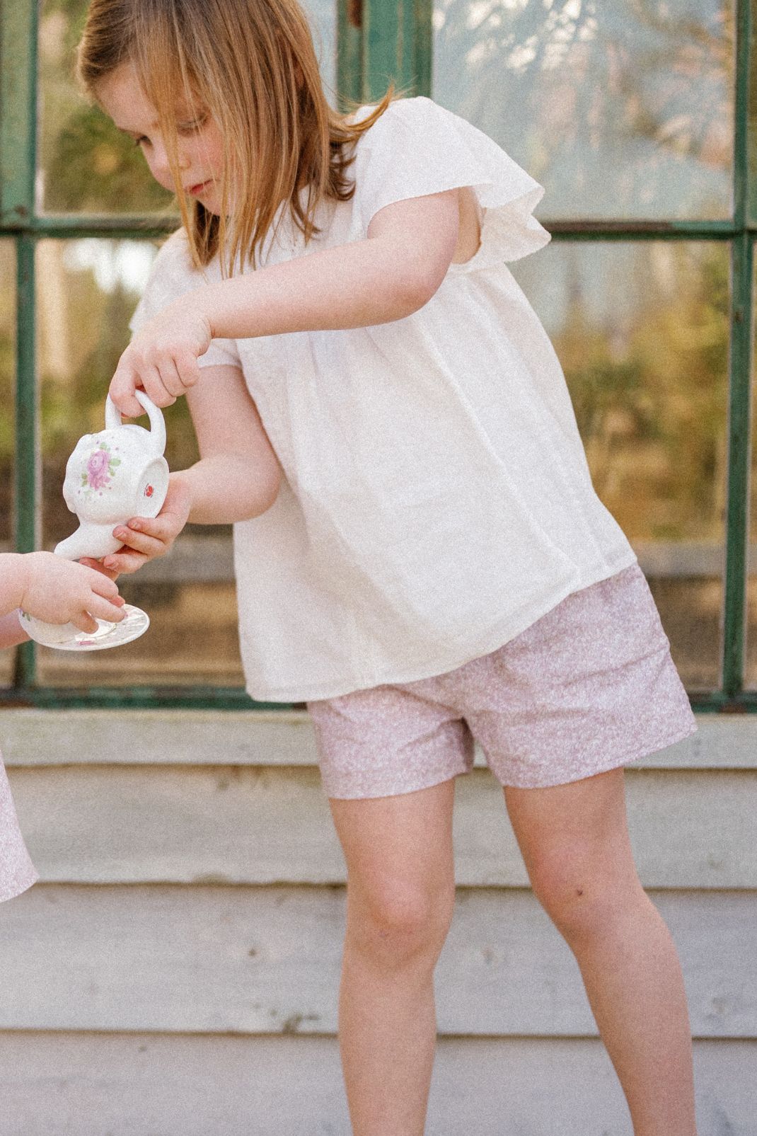 Lifestyle shot of a little girl pouring a tea pot wearing our Mae Short in Scattered Blooms